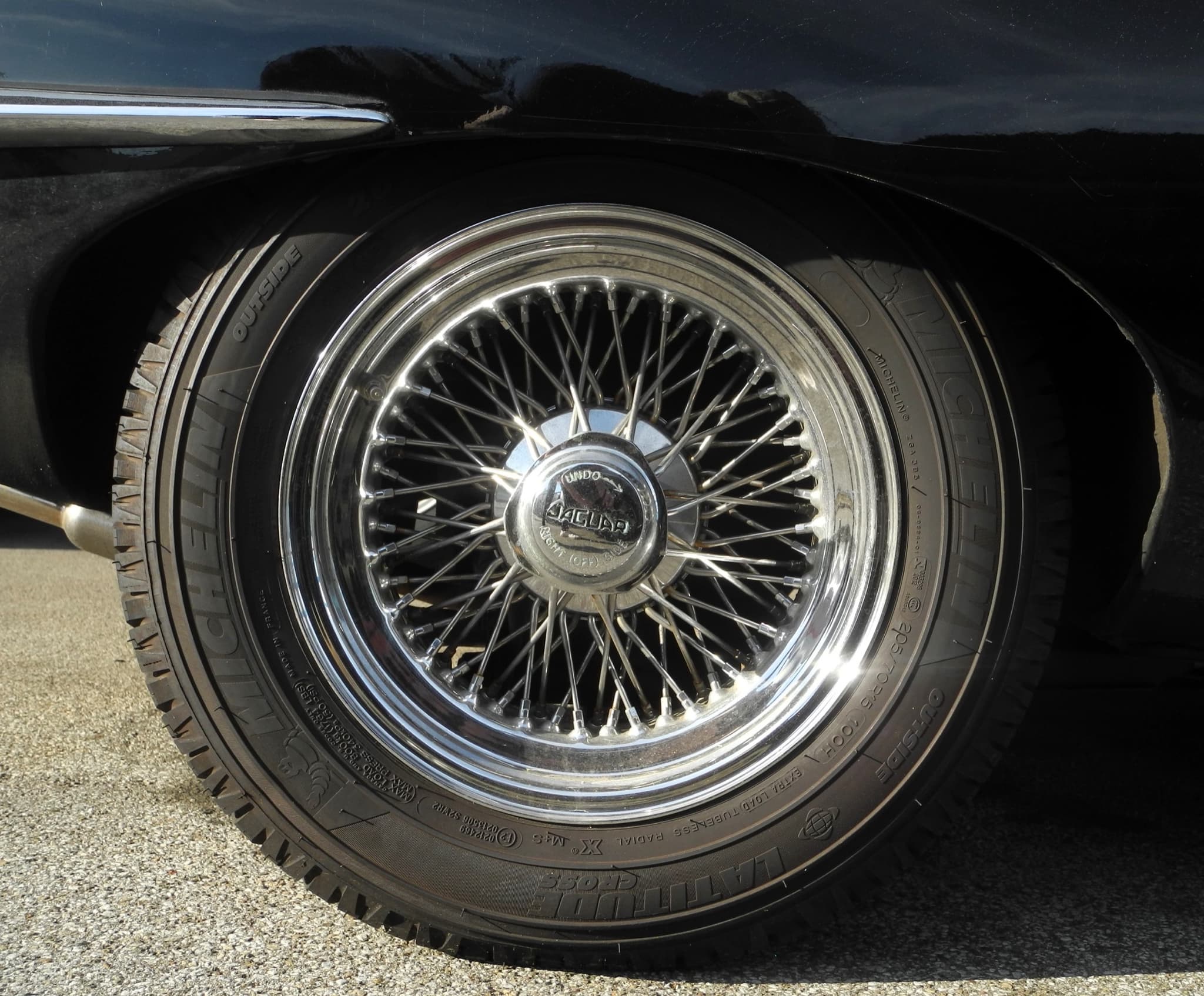 A wire wheel with an octagonal chrome hub cap marked 'JAGUAR', without ears, on a black E-Type. Opens a larger view