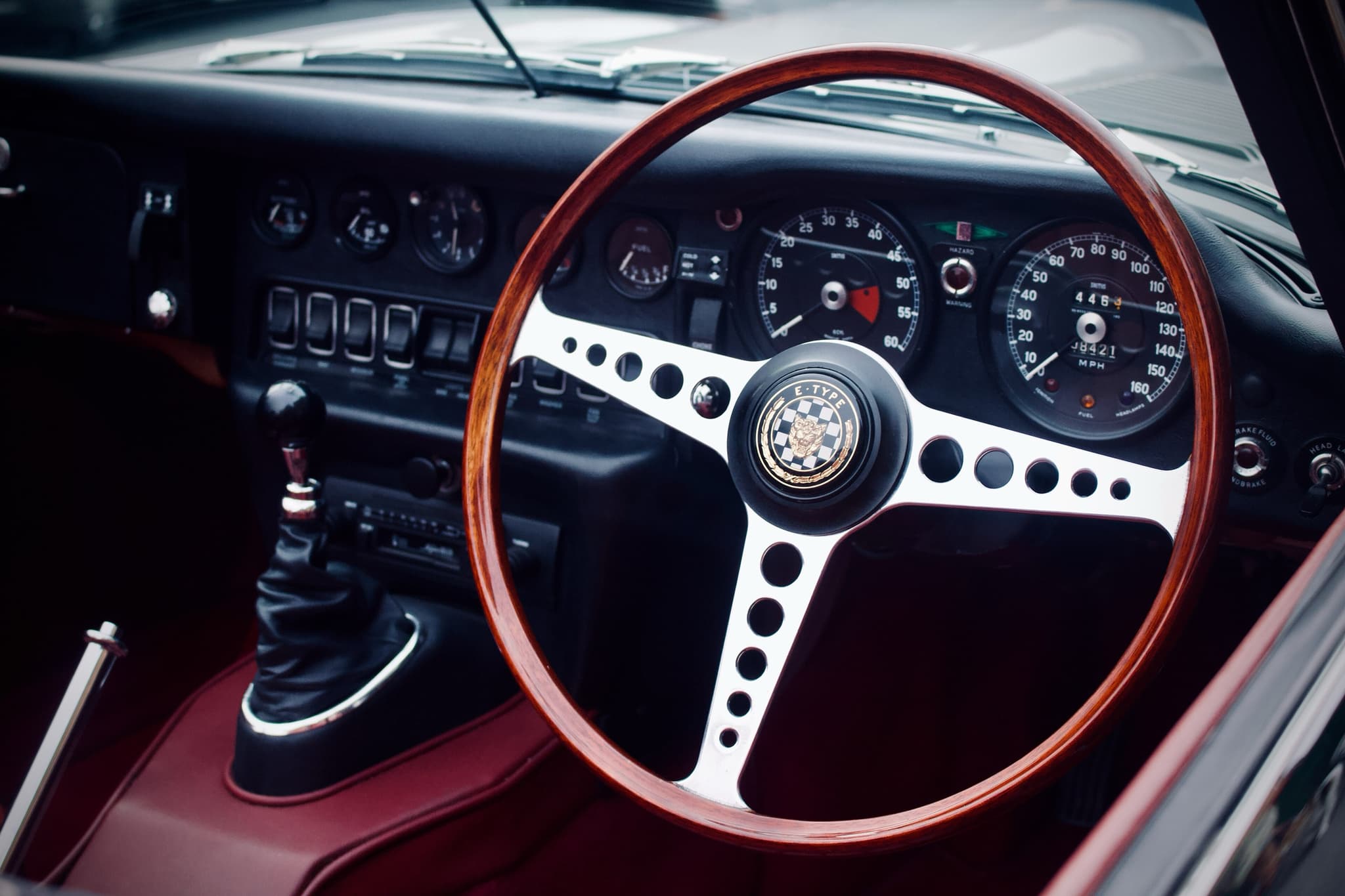 The dash of an E-Type roadster: a wood-rim wheel, two large dials and a black centre panel with rocker switches.