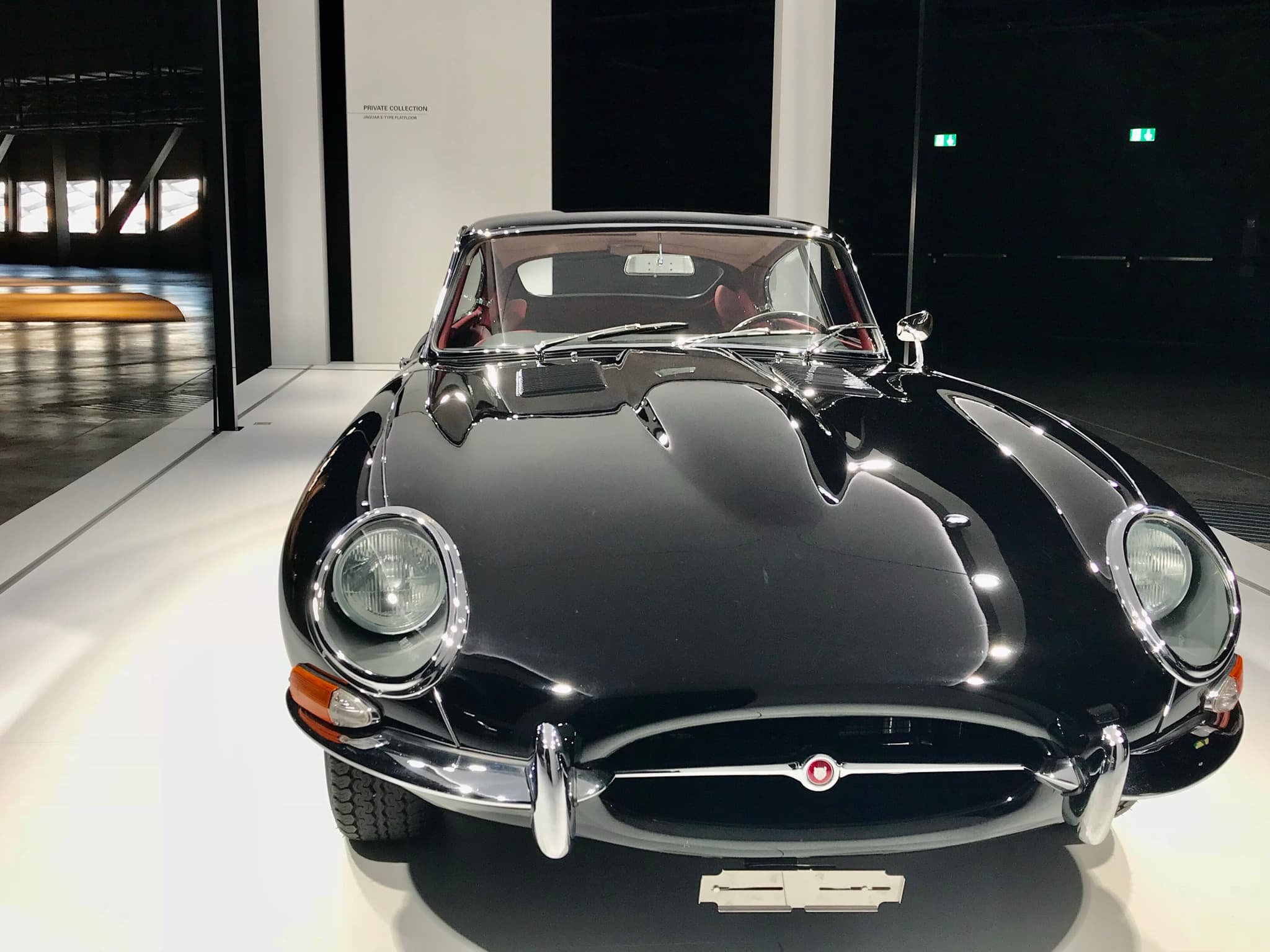 A black E-Type coupé seen head-on from slightly above, with glass-covered headlamps and a small oval intake.