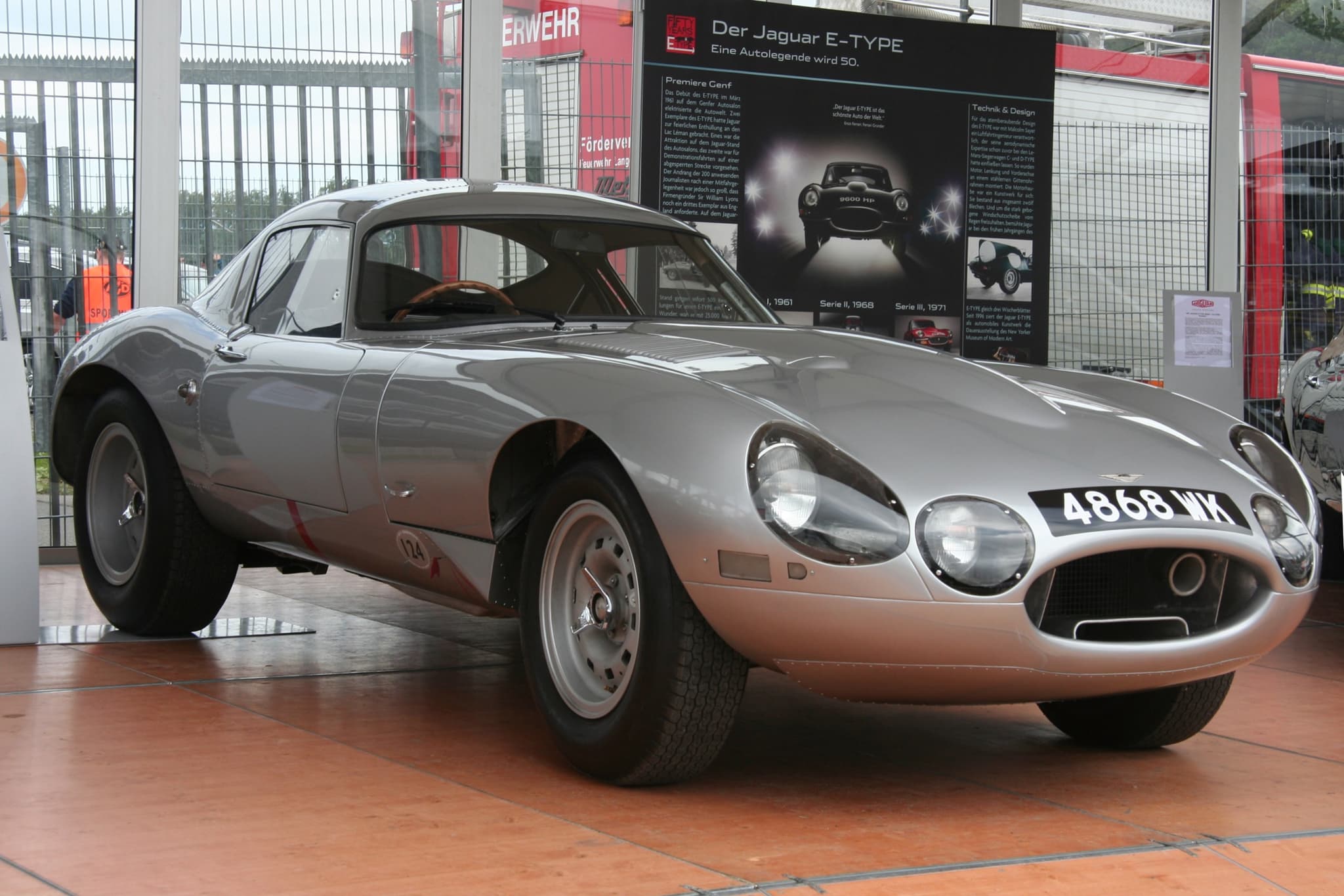 A silver low-drag E-Type coupé with three headlamp openings and the registration 4868 WK on a display stand. Opens a larger view