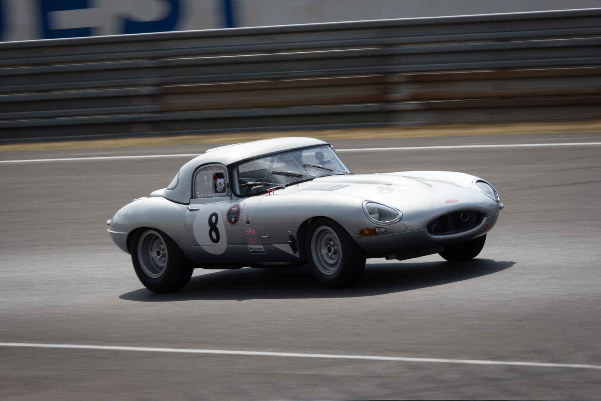 A silver E-Type with a hardtop and the number 8 cornering at speed.