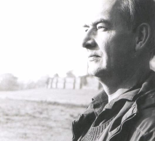A black-and-white profile portrait of a grey-haired man in a jacket, looking into the distance. Opens a larger view