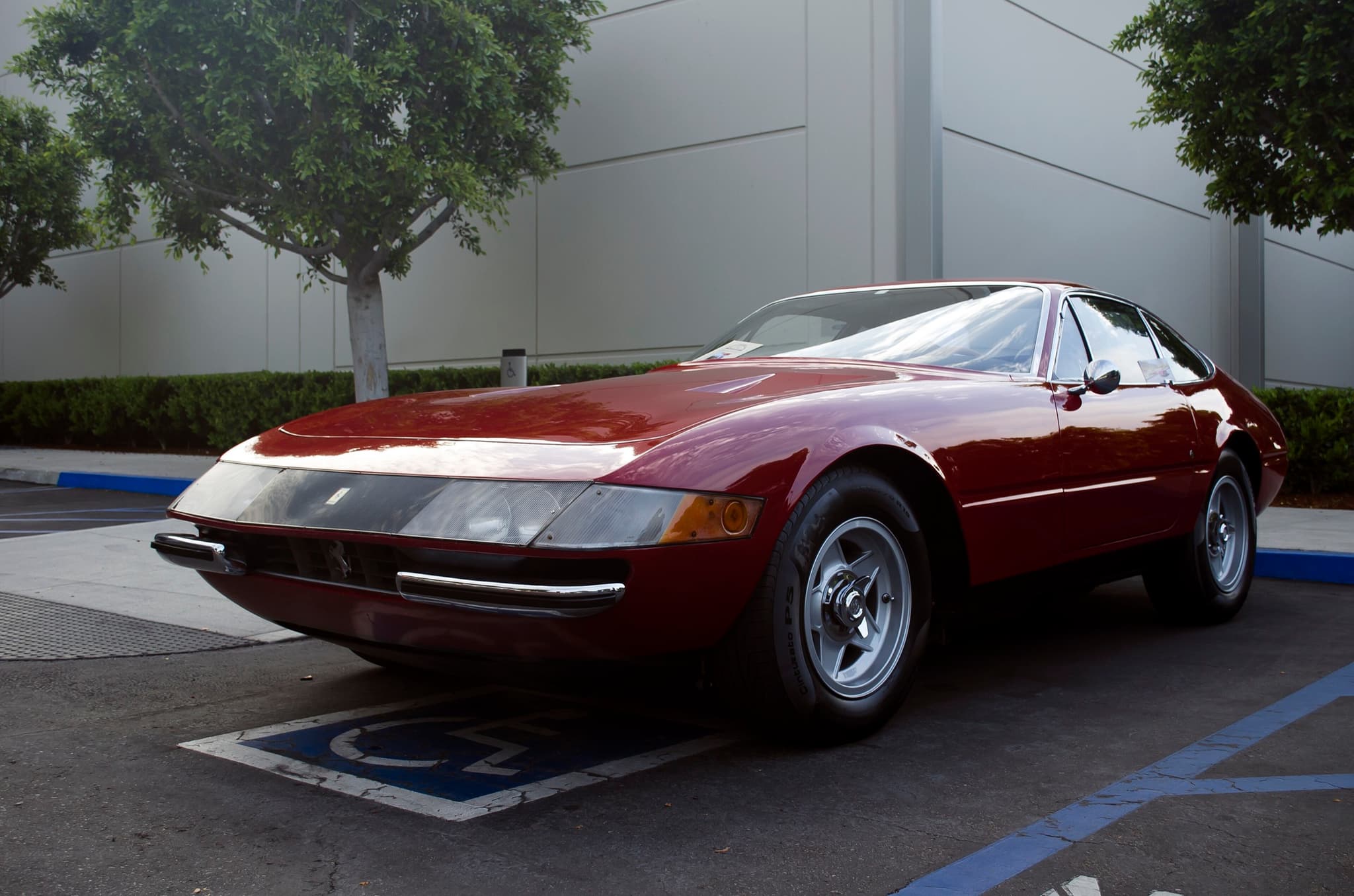 A maroon Ferrari 365 GTB/4 Daytona with covered headlamps in a car park.