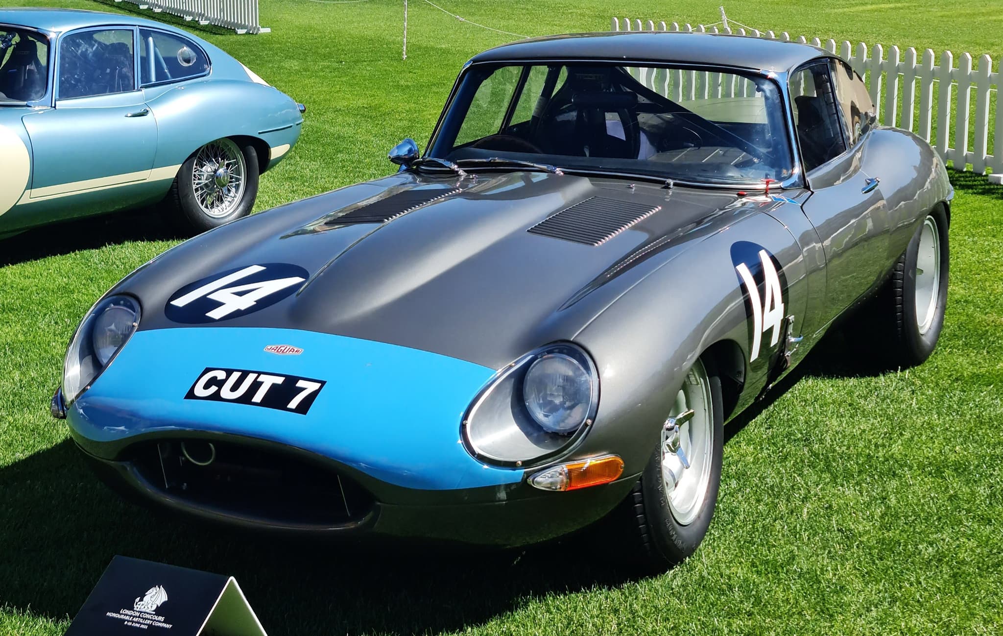 A grey E-Type coupé with a light blue nose band, the number 14 and the registration CUT 7 on grass.