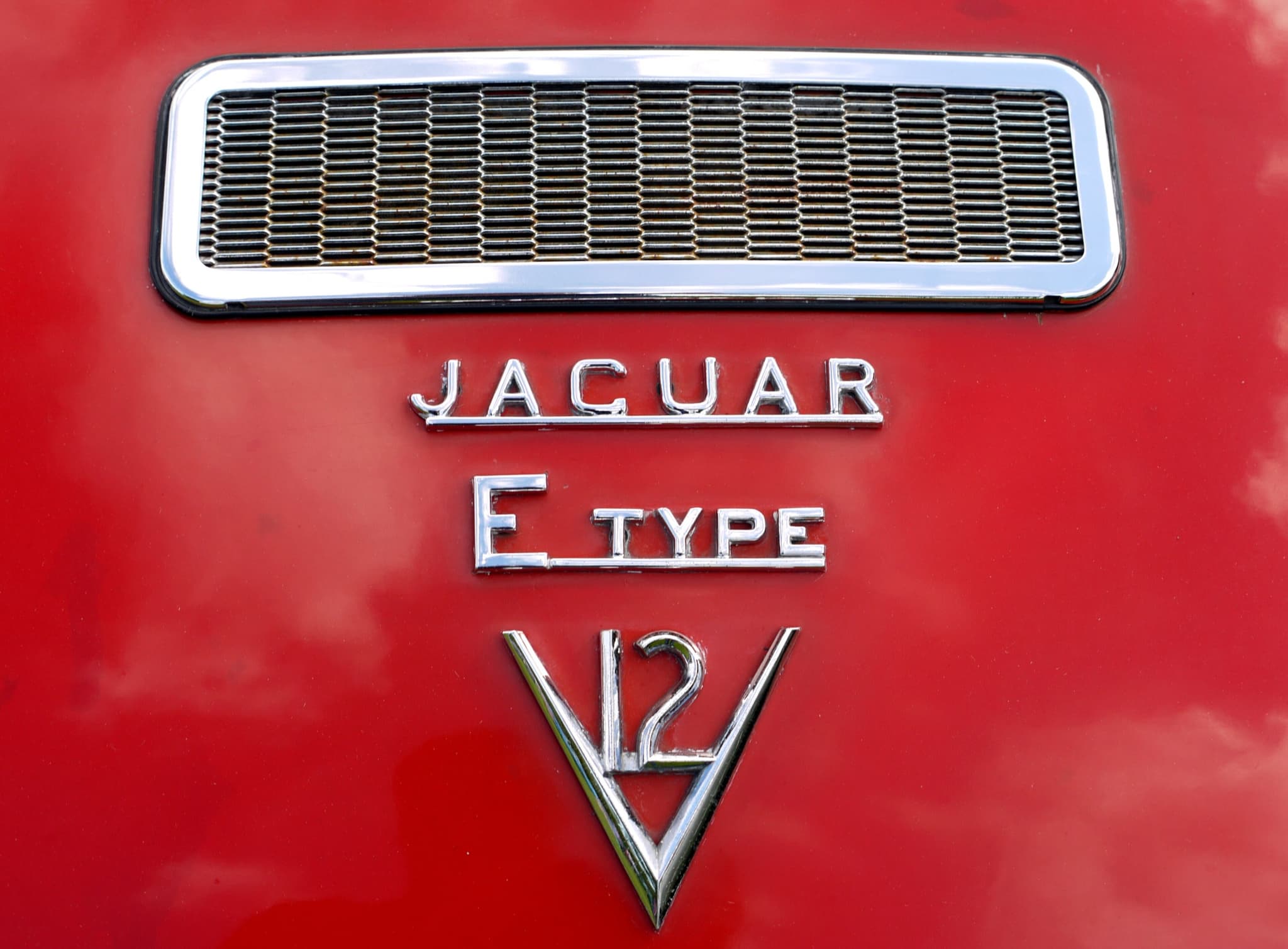 Chrome 'JAGUAR', 'E TYPE' and V-shaped 'V12' badges below a vent grille on a red tailgate. Opens a larger view