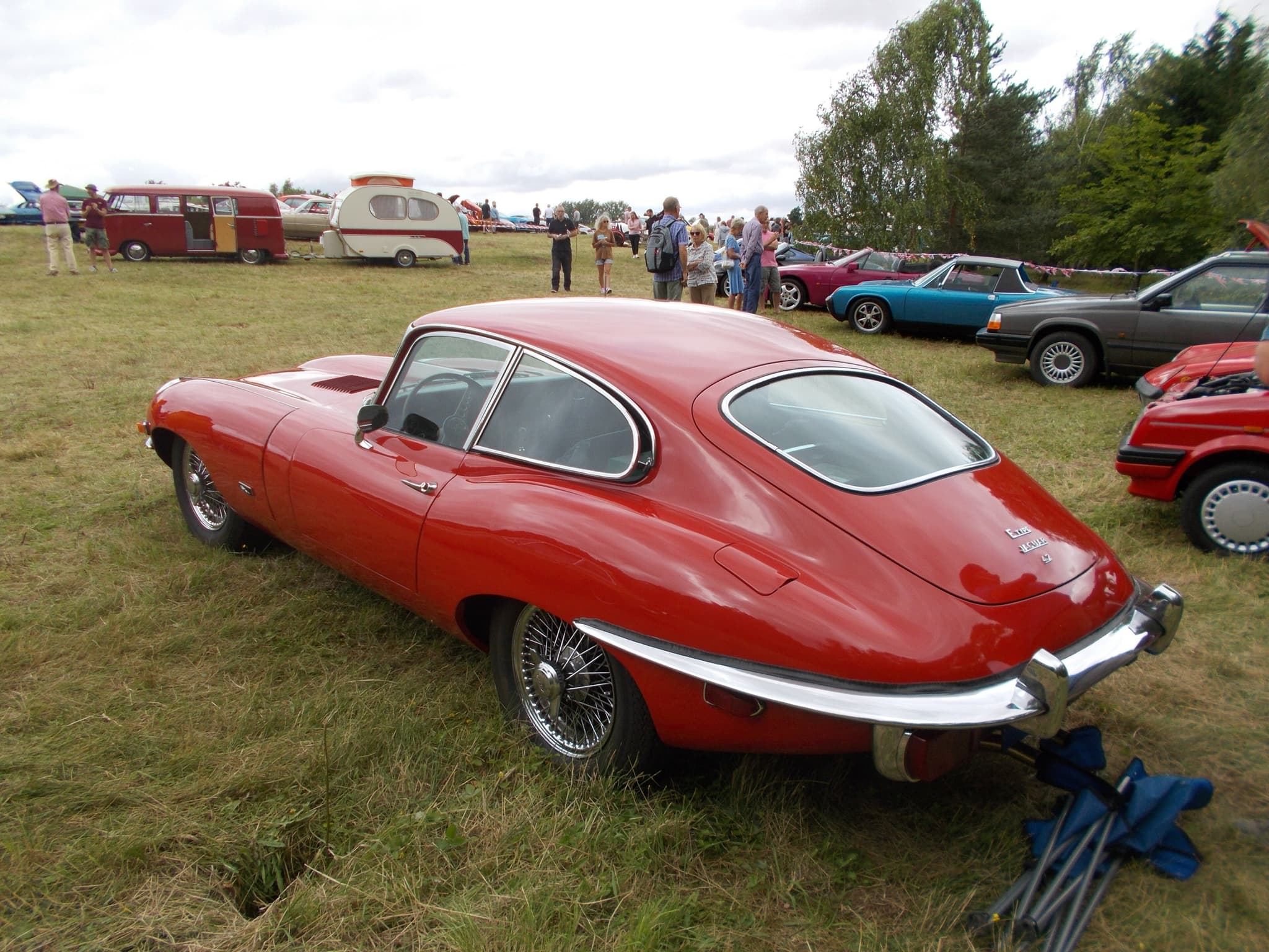 A red E-Type coupé from behind on a show field, its large tail lamps below a raised wrap-round bumper.