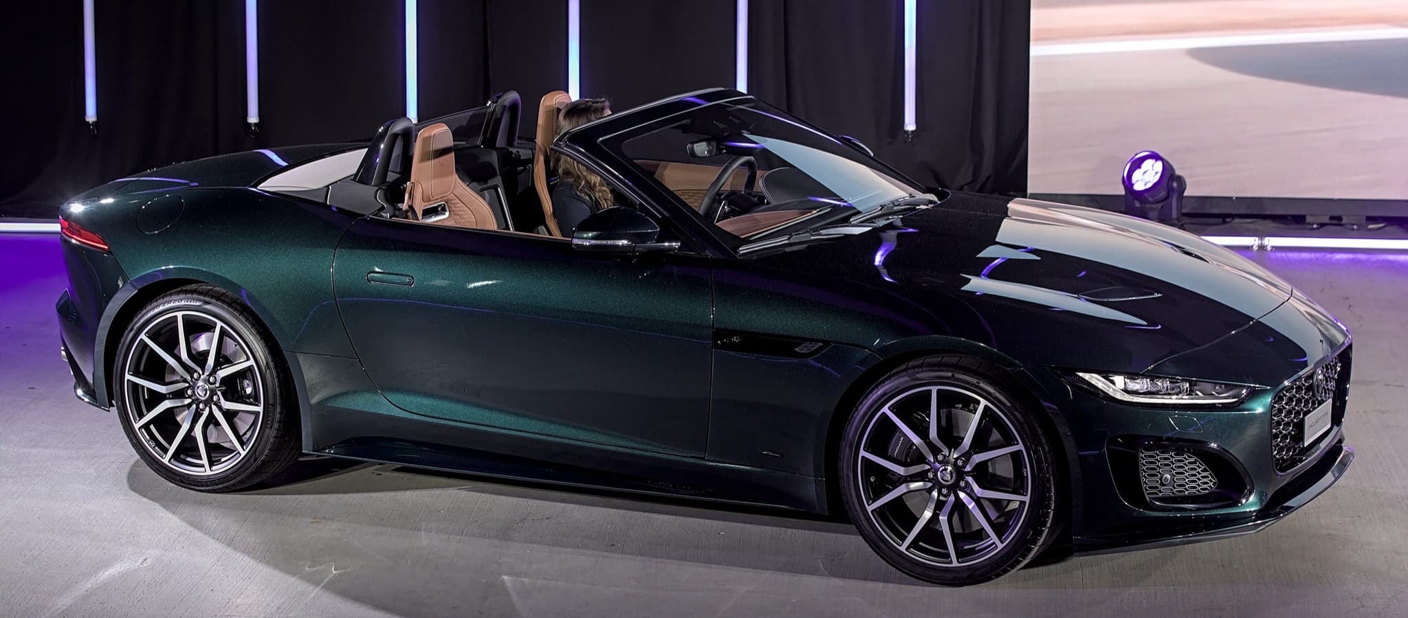 A dark green Jaguar F-Type convertible with its roof down on a show stage.