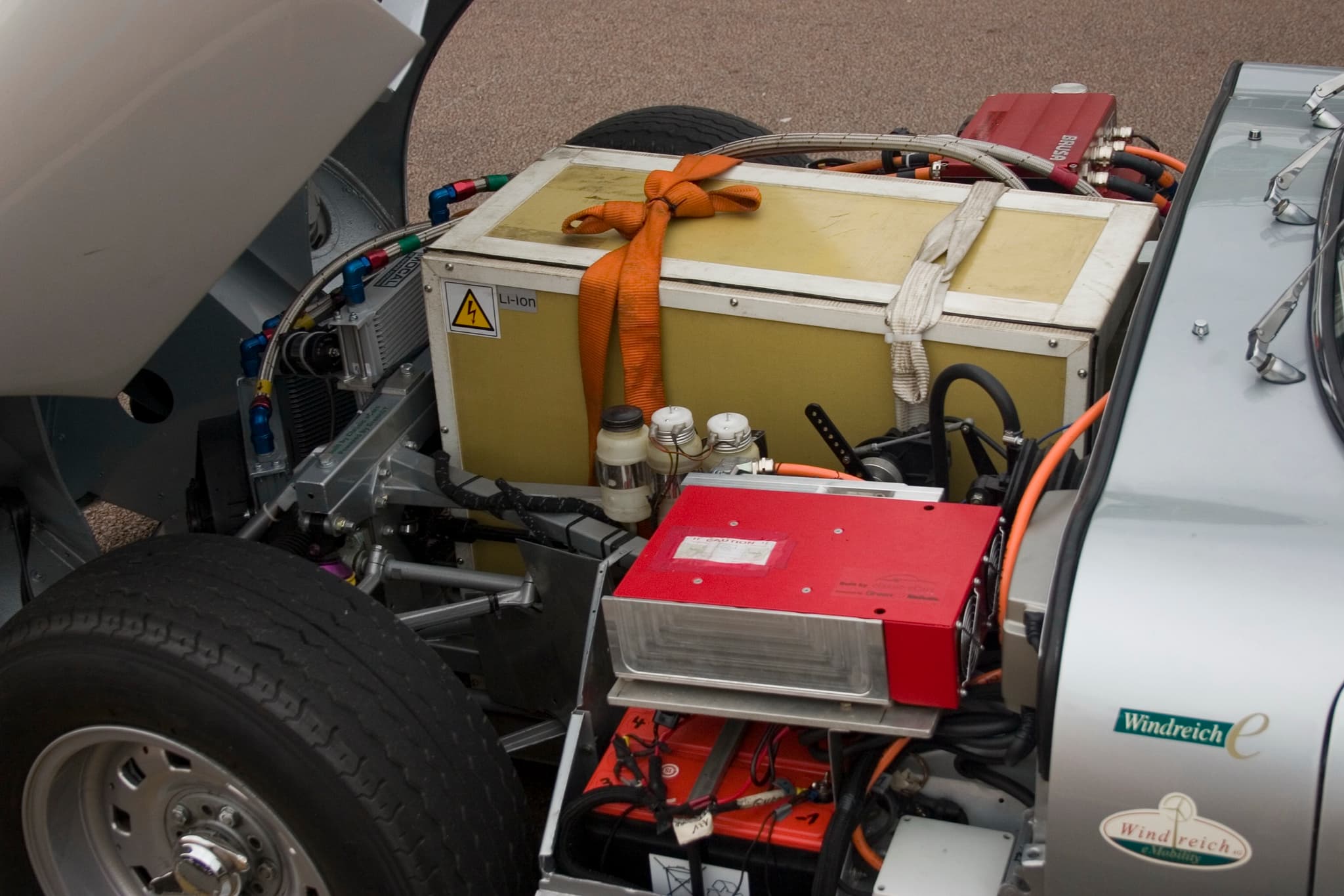 Under an E-Type's tipped-forward bonnet: a yellow lithium-ion battery box, a red controller and orange cables in place of the engine.