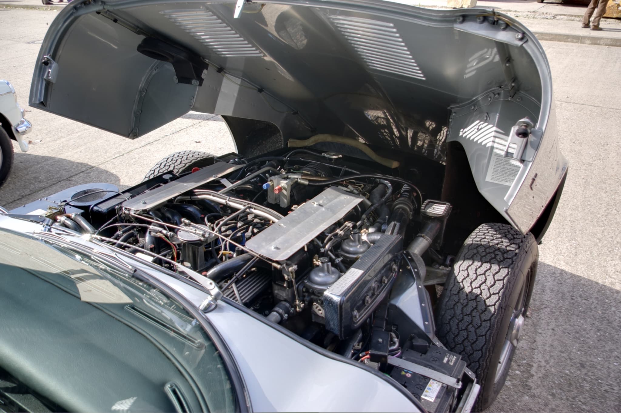 A V12 engine filling an E-Type's engine bay under the tipped-forward bonnet.