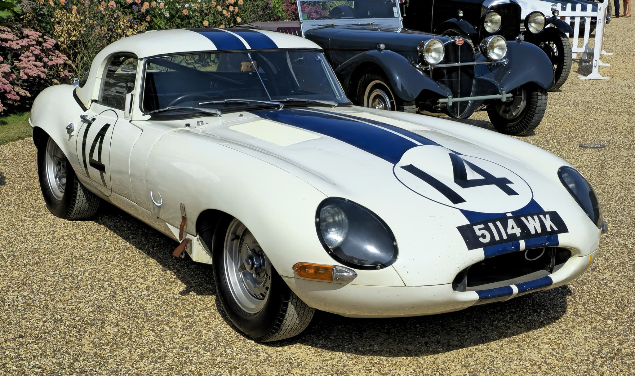 A white E-Type Lightweight with two blue stripes, the number 14 and the registration 5114 WK on gravel.