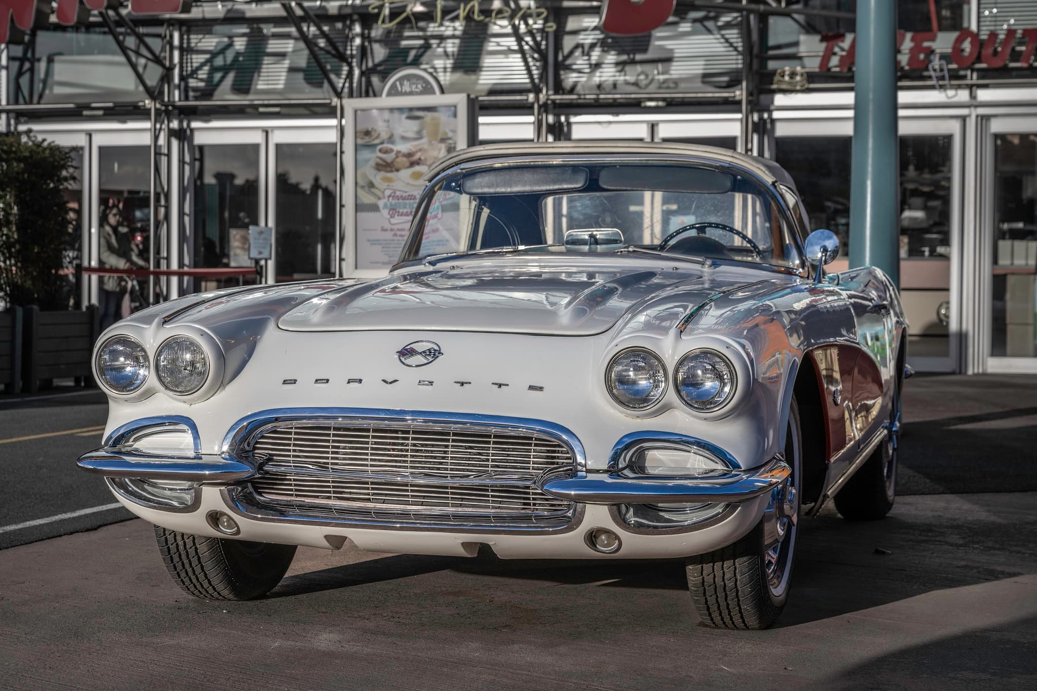 A silver early-1960s Chevrolet Corvette with a hardtop, seen head-on in front of a glass building.