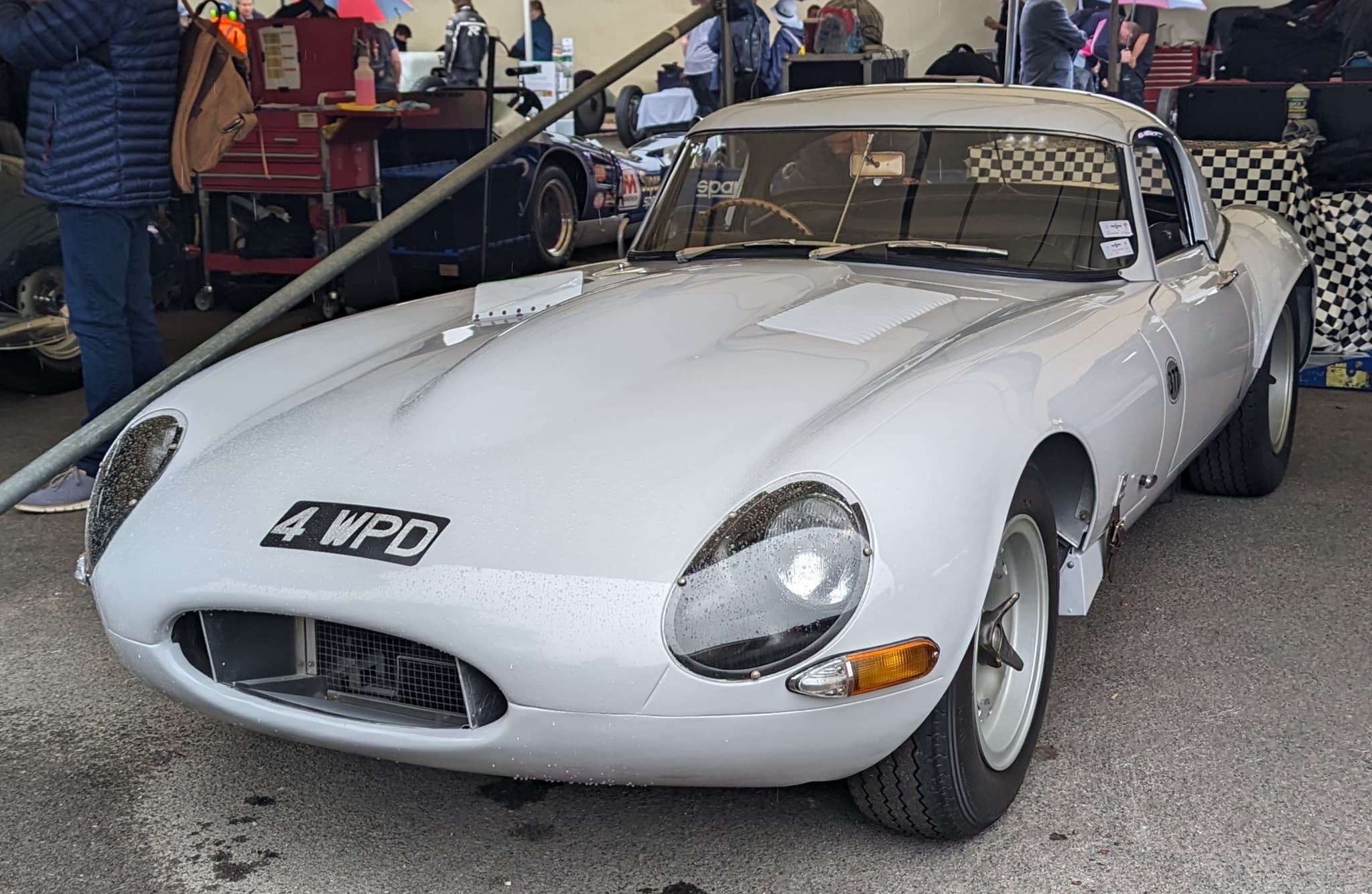 The front of a white E-Type Lightweight with the registration 4 WPD under a paddock awning. Opens a larger view