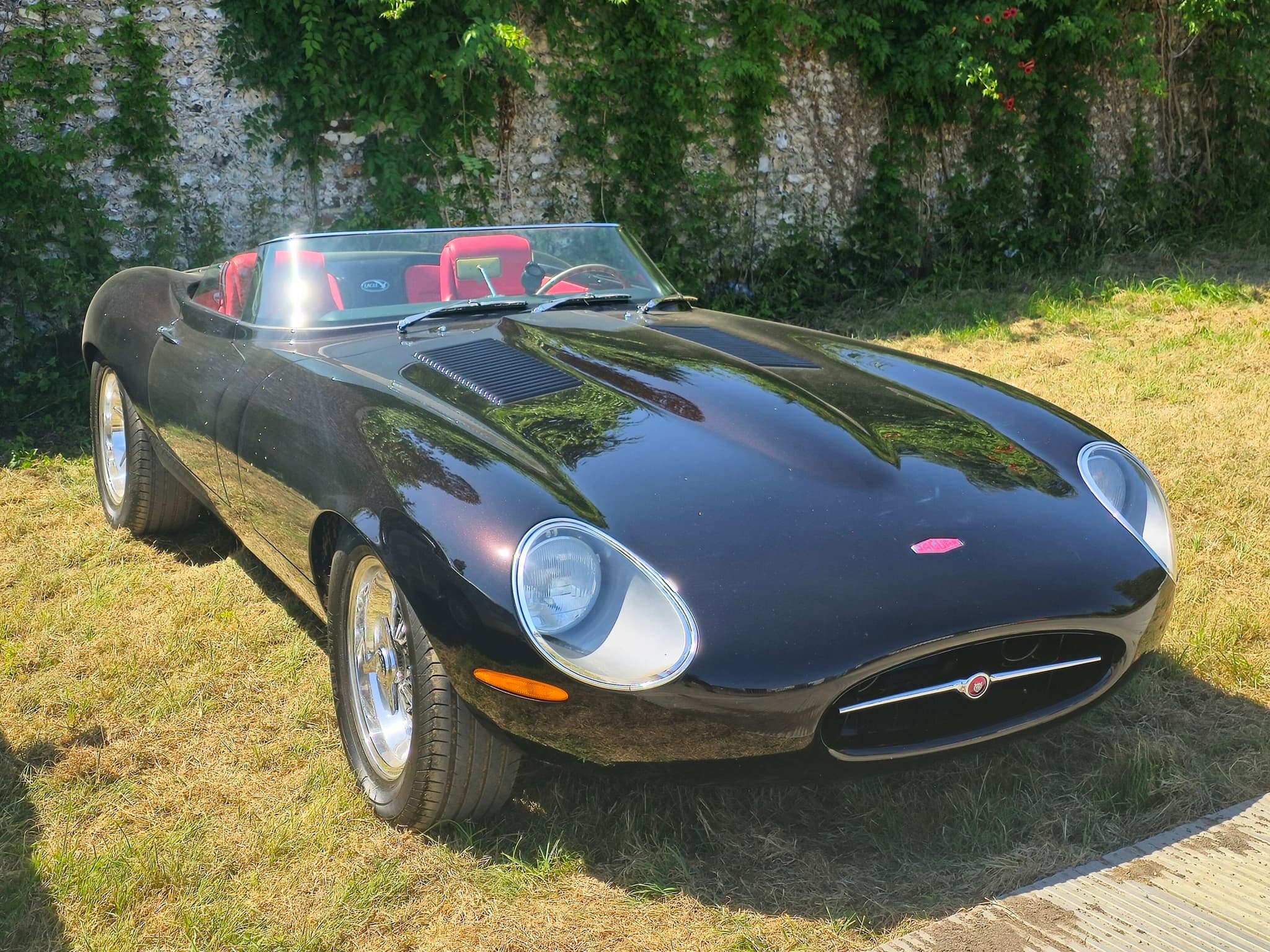 A black Eagle Speedster with a low raked screen and red seats, parked on grass before a flint wall.
