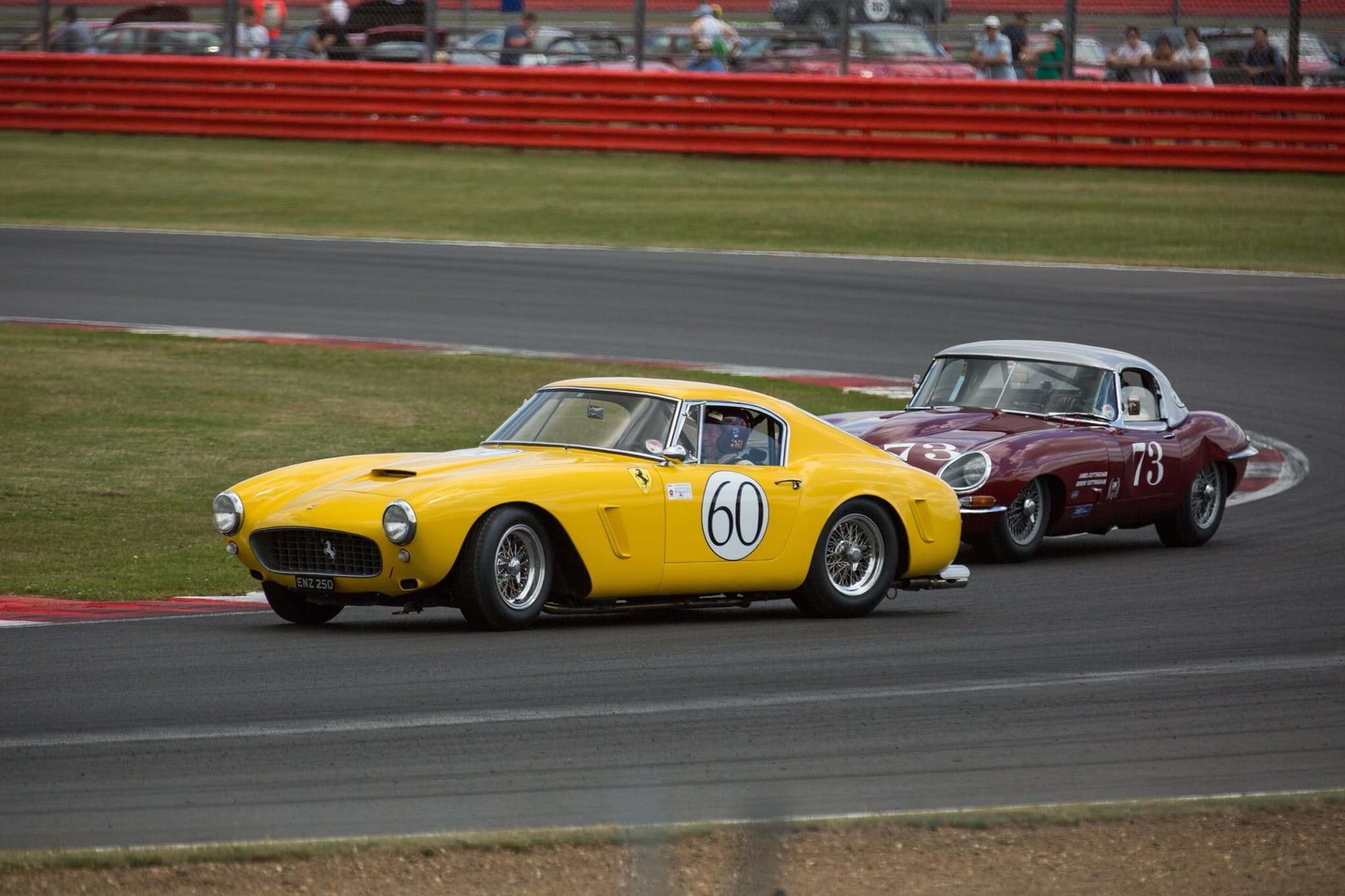 A yellow Ferrari 250 GT SWB leading a maroon E-Type with a white hardtop through a corner.