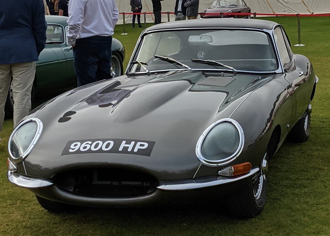 The front of a grey E-Type coupé with the registration 9600 HP on grass, a green E-Type behind.