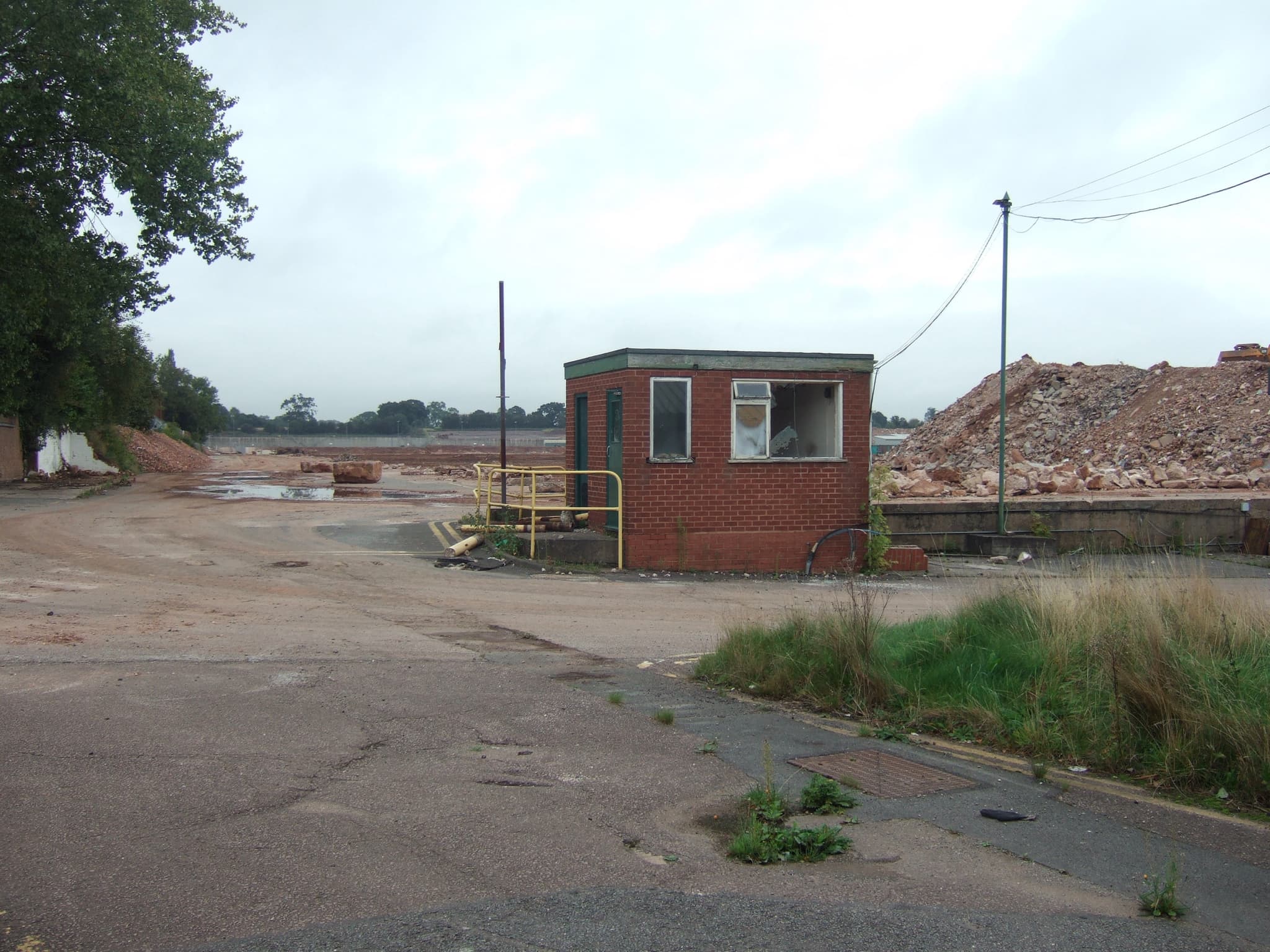 A demolition site with heaps of rubble and a small brick gatehouse.