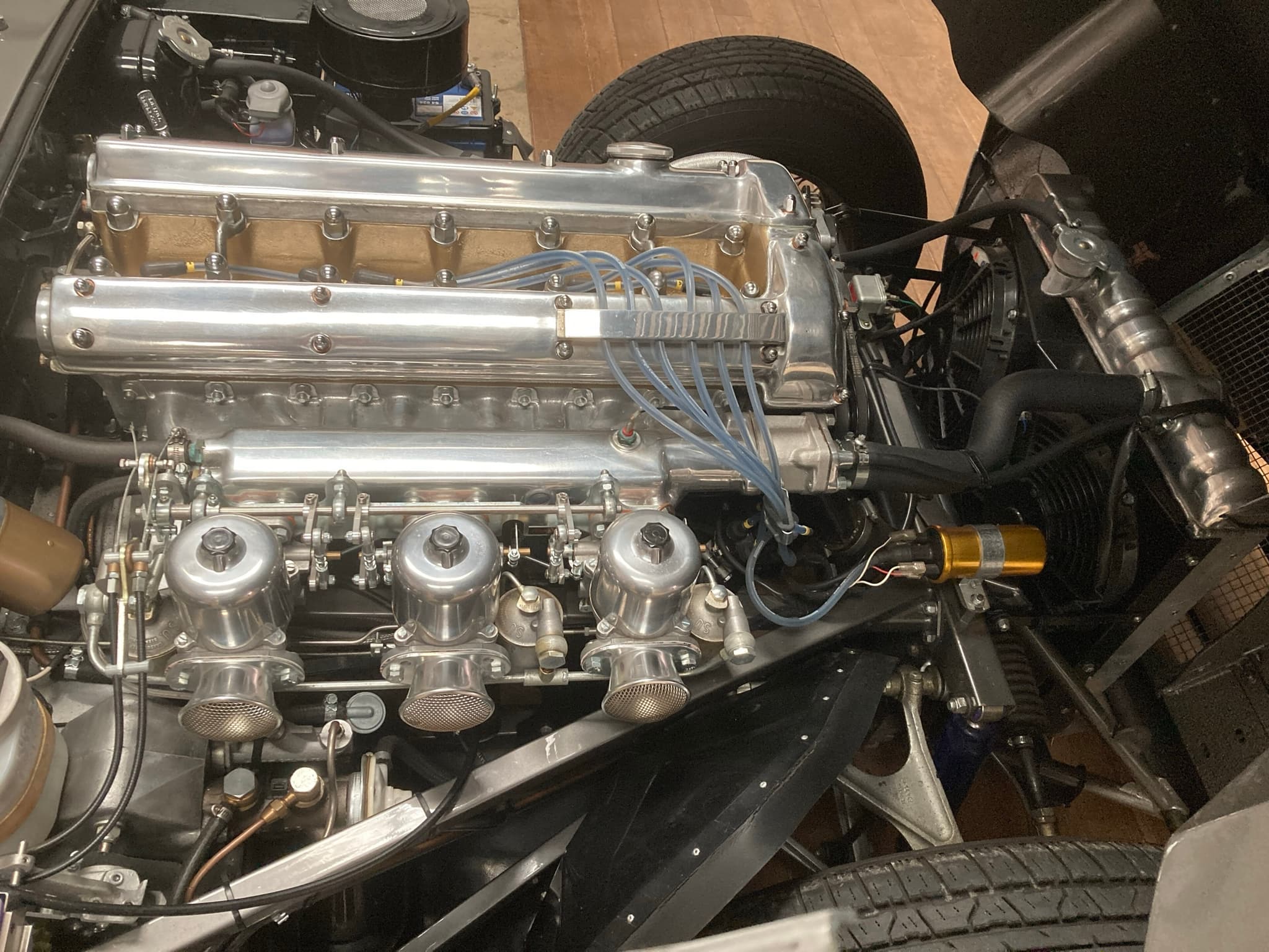 An E-Type's six-cylinder engine from above, with polished cam covers, blue ignition leads and three carburettors.