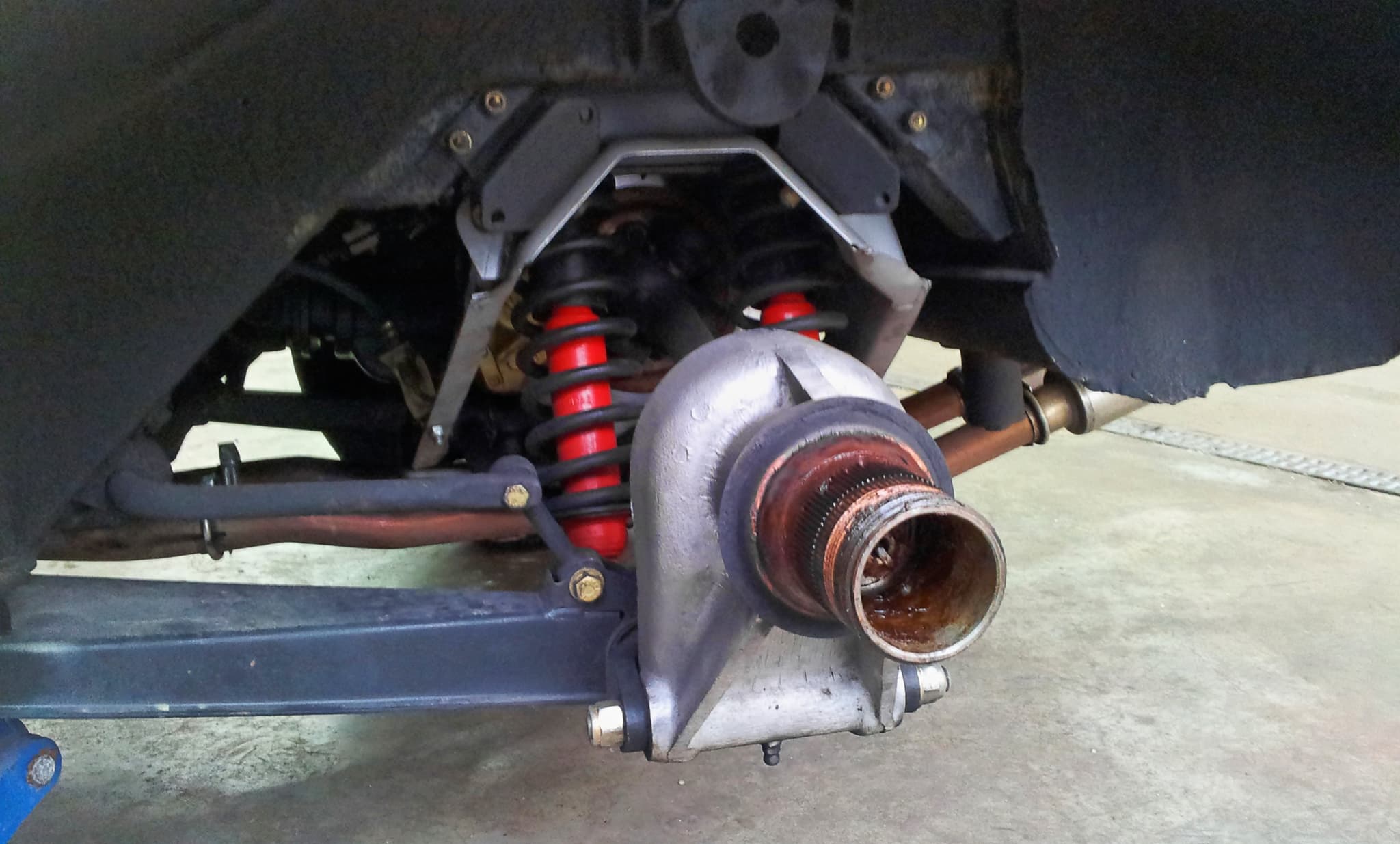 The rear suspension of an E-Type on a lift: a hub carrier, twin red coil-spring dampers and a drive shaft.